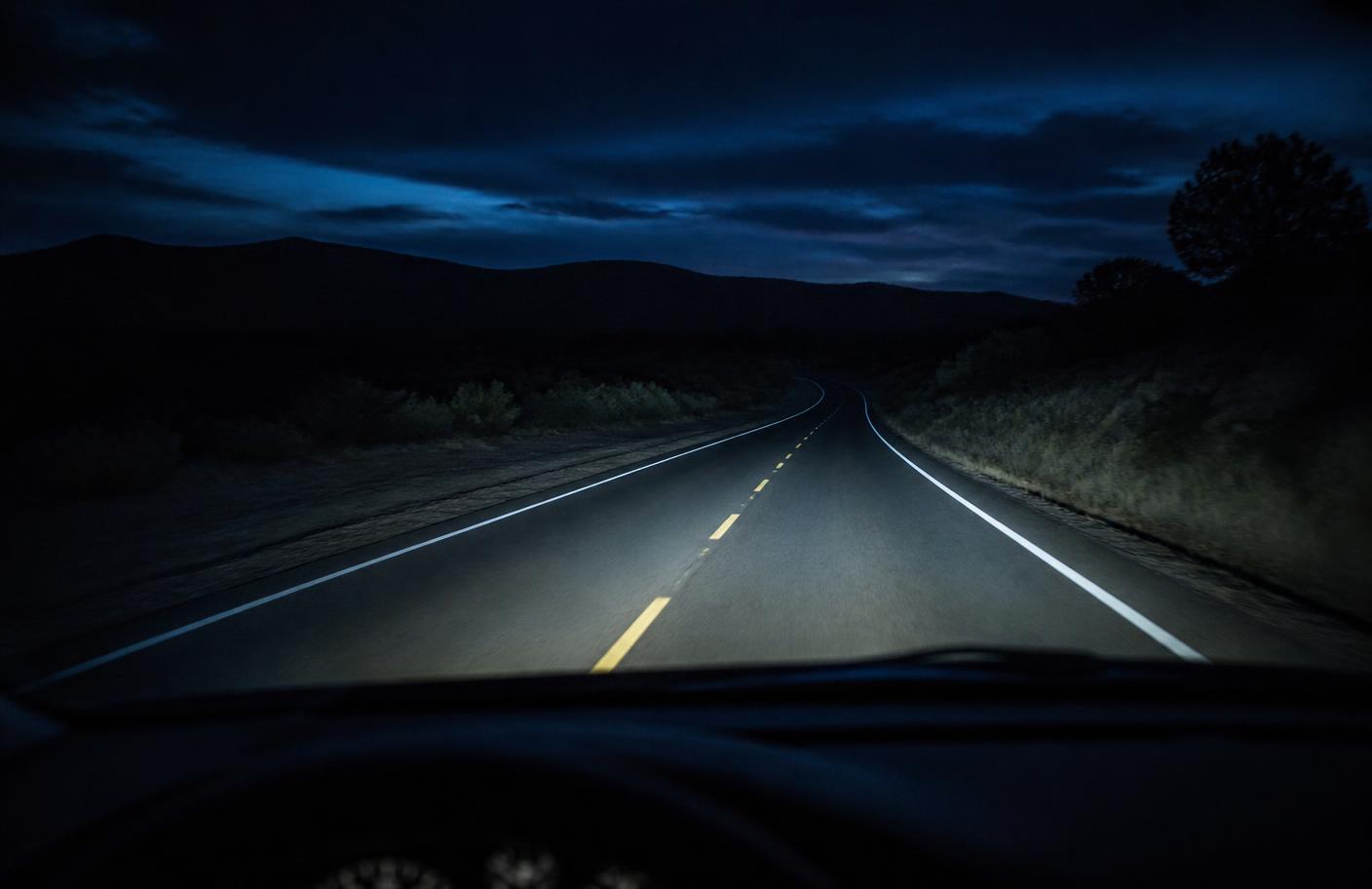 An empty country road at night, seen through a car windshield